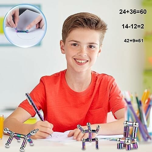 Smiling boy in red shirt playing with magnetic toys at a desk.