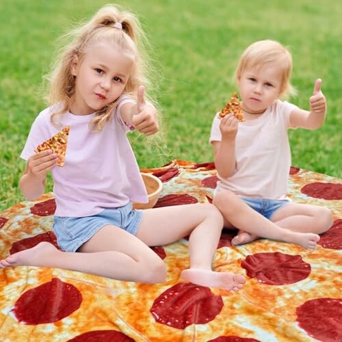 Two children sitting on a pizza blanket, holding slices and giving thumbs up.