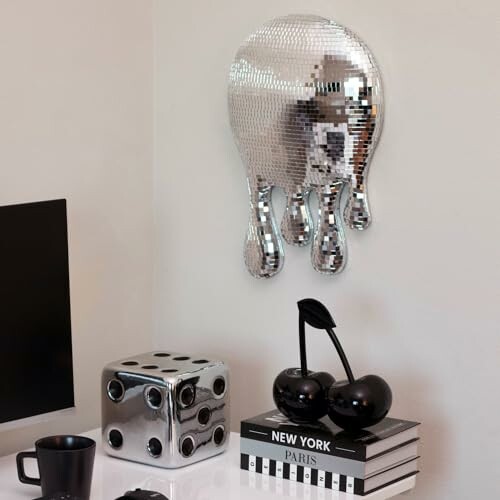 Contemporary office decor with a mirrored wall sculpture, a large dice, black cherries, and books.